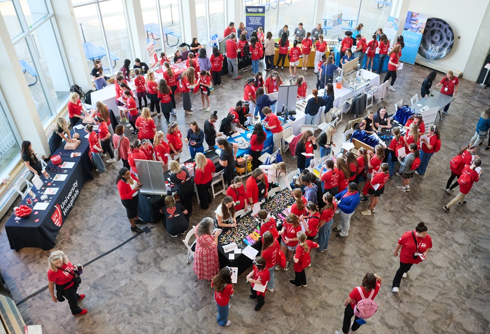 Overhead view of educational stations with girls in red shirts crowded throughout.